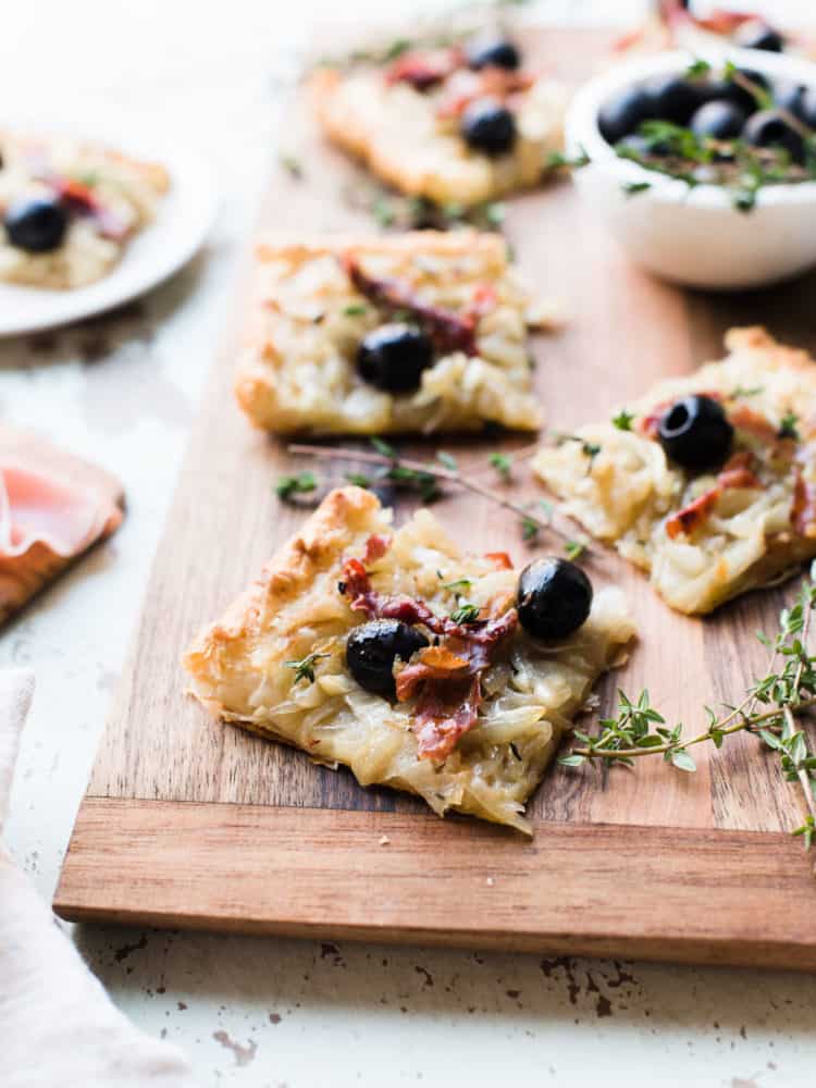 Slices of homemade Pissaladière with Prosciutto on a wooden serving board.