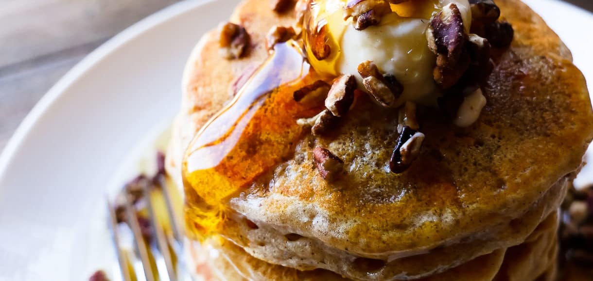 Stack of sweet potato pancakes with maple syrup pouring on top.