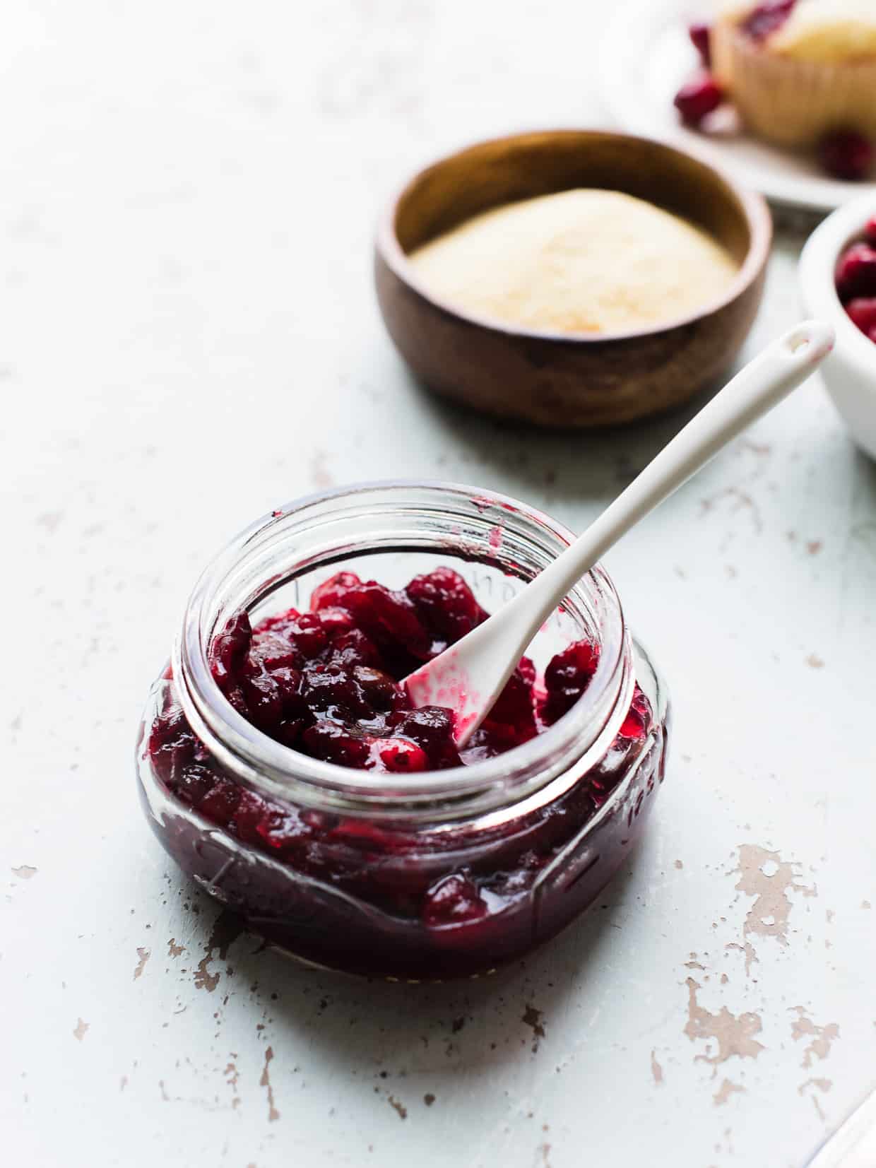 Glass jar of cranberry sauce on a rustic counter top.
