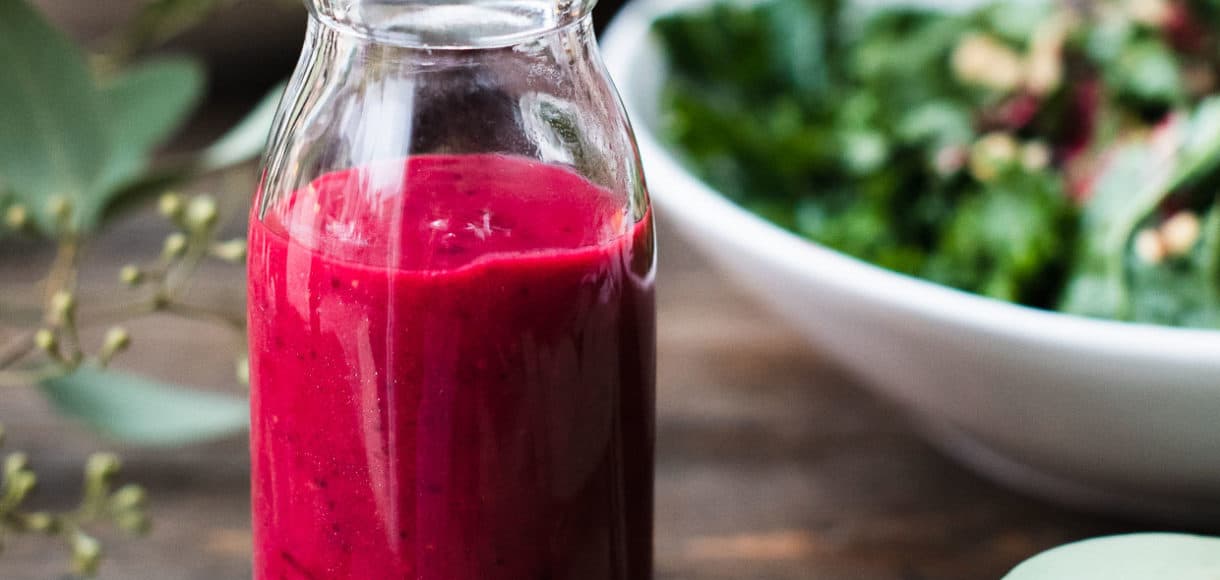 Small glass bottle of Cranberry Sauce Vinaigrette with a green salad in the background.