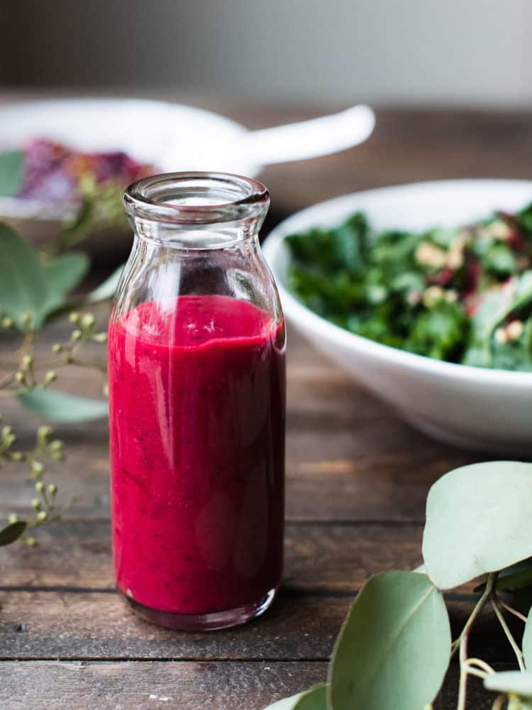 Small glass bottle of Cranberry Sauce Vinaigrette with a green salad in the background.