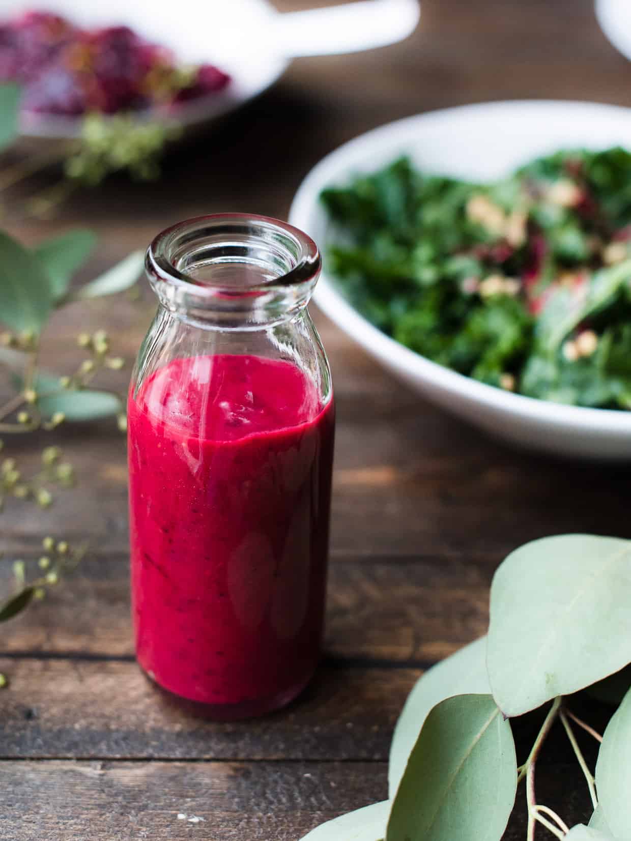 Glass bottle of Cranberry Sauce Vinaigrette with a green salad in the background.