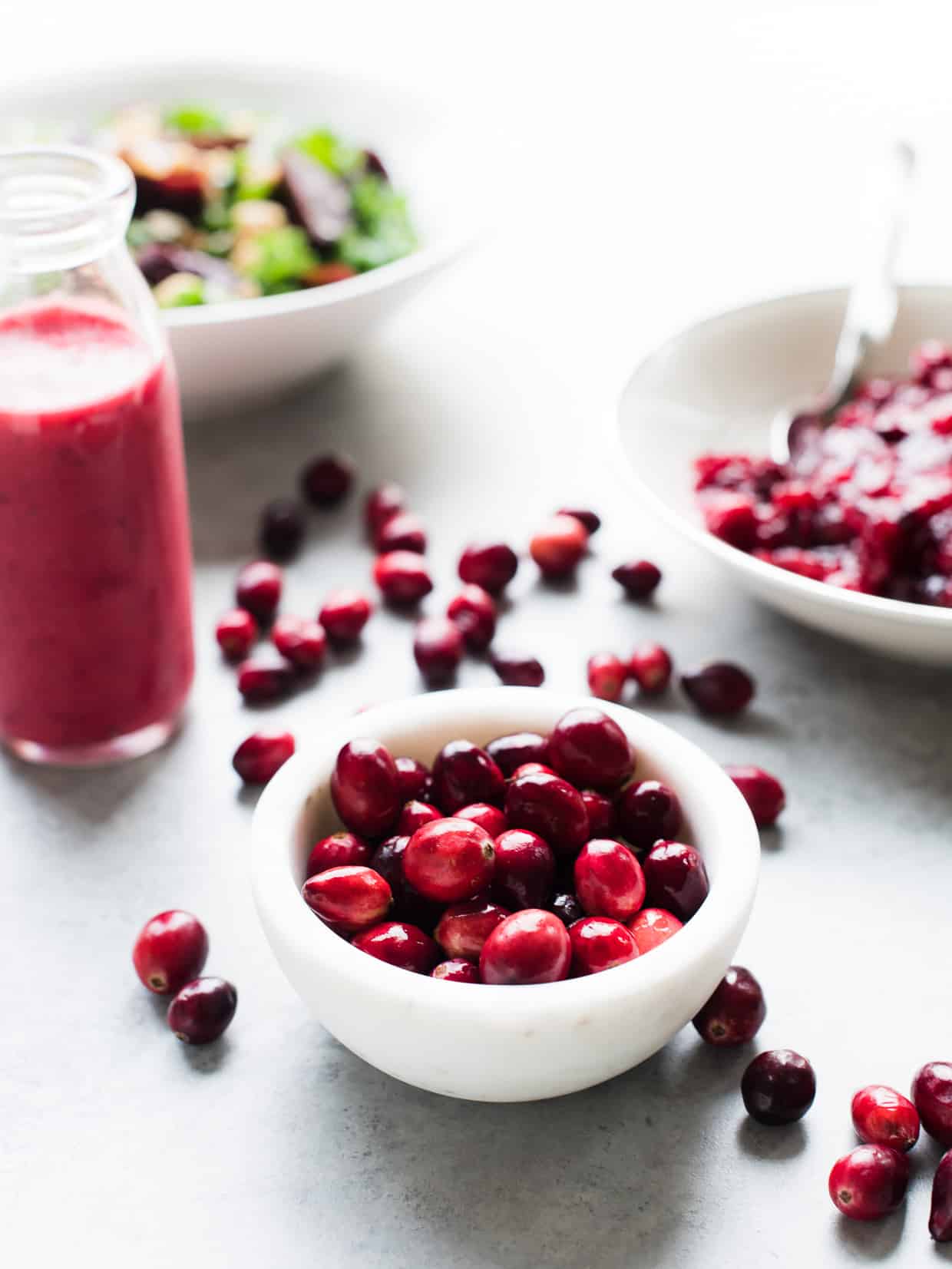 White bowl filled with fresh cranberries with a cranberry sauce vinaigrette in the background.