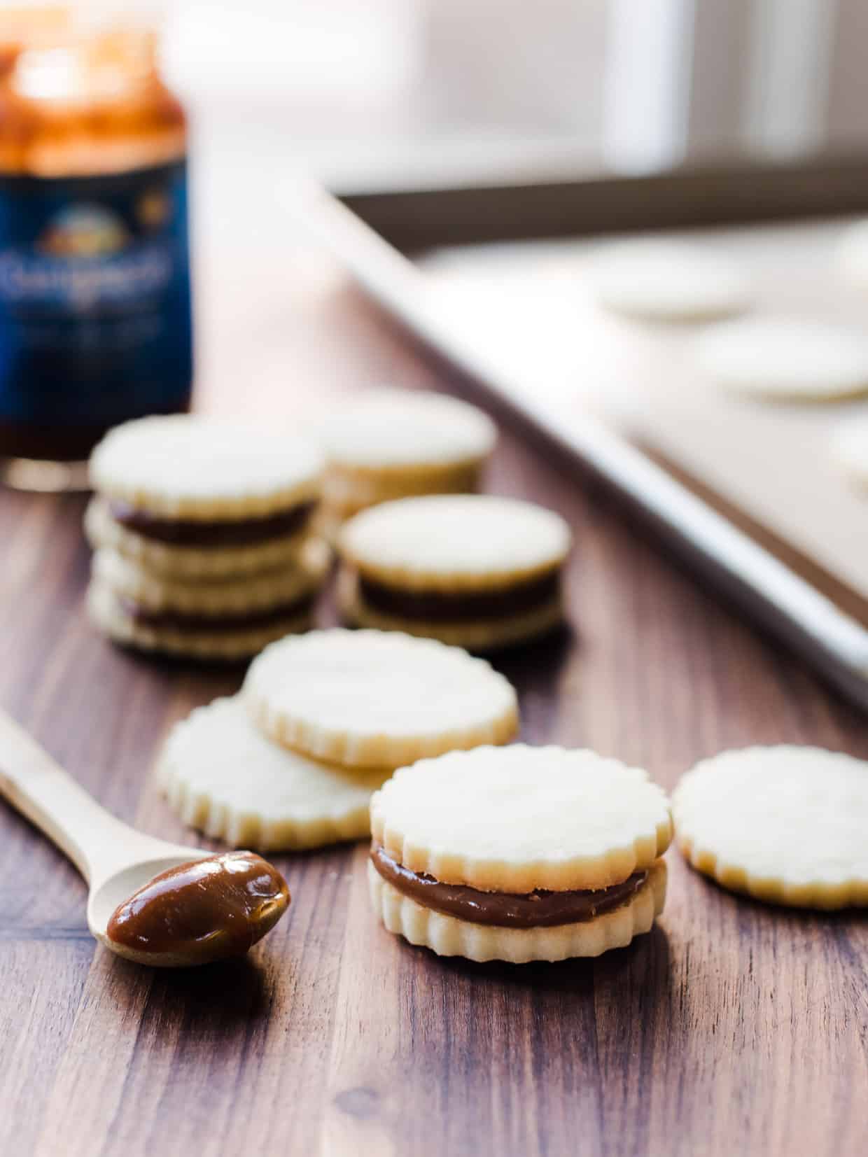 Spoon filled with dulce de leche surrounded by Alfajores cookies.