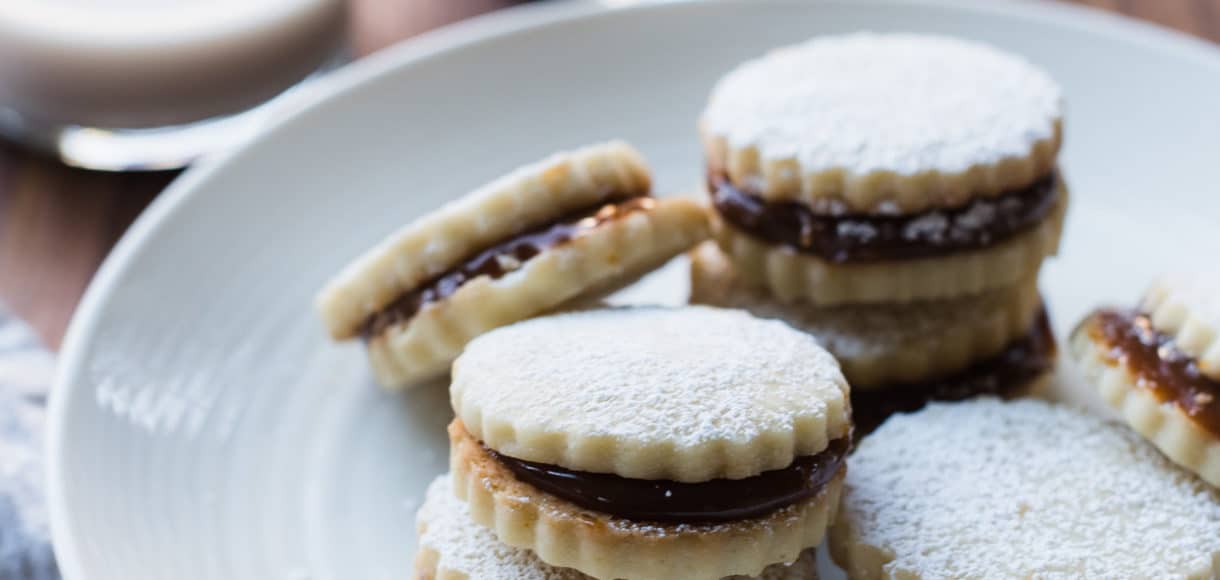 Alfajores on a white plate with two glasses of milk in the background.