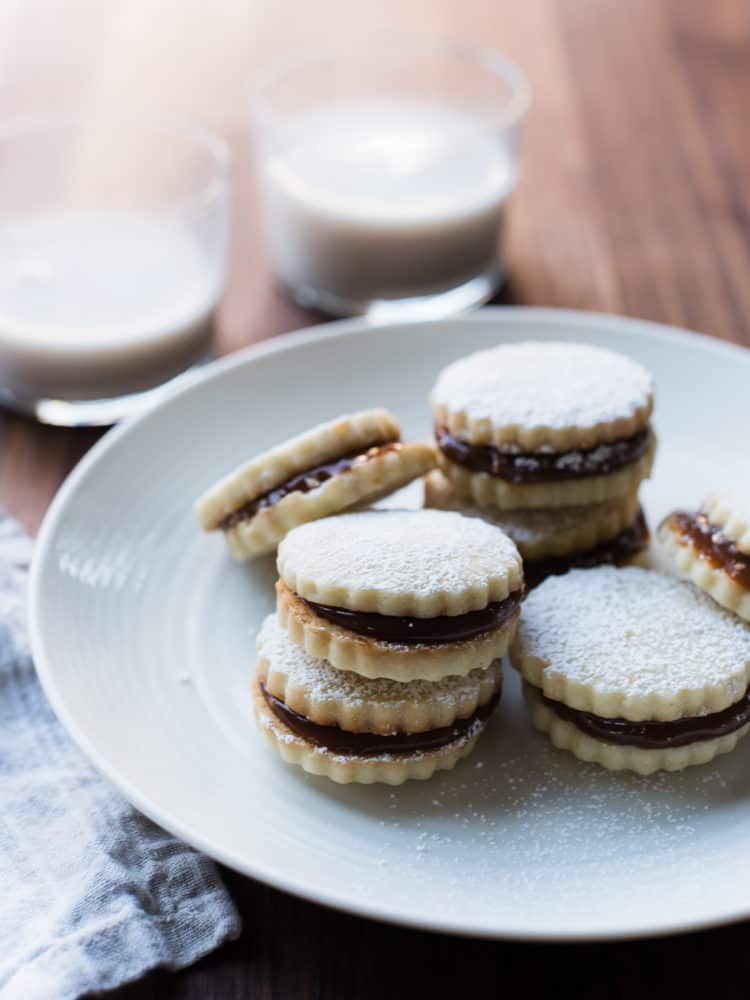 Alfajores on a white plate with two glasses of milk in the background.