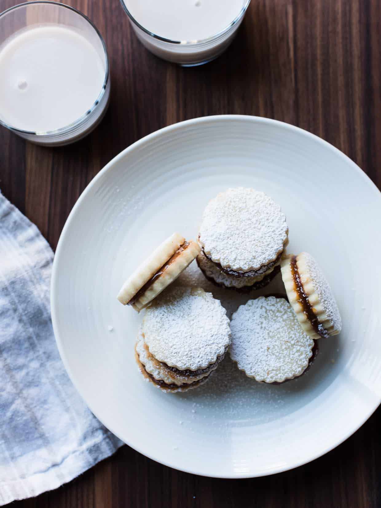 Alfajores on a white plate with two glasses of milk in the background.