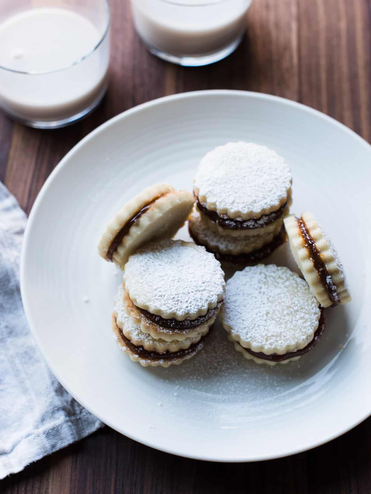 Alfajores on a white plate with two glasses of milk in the background.