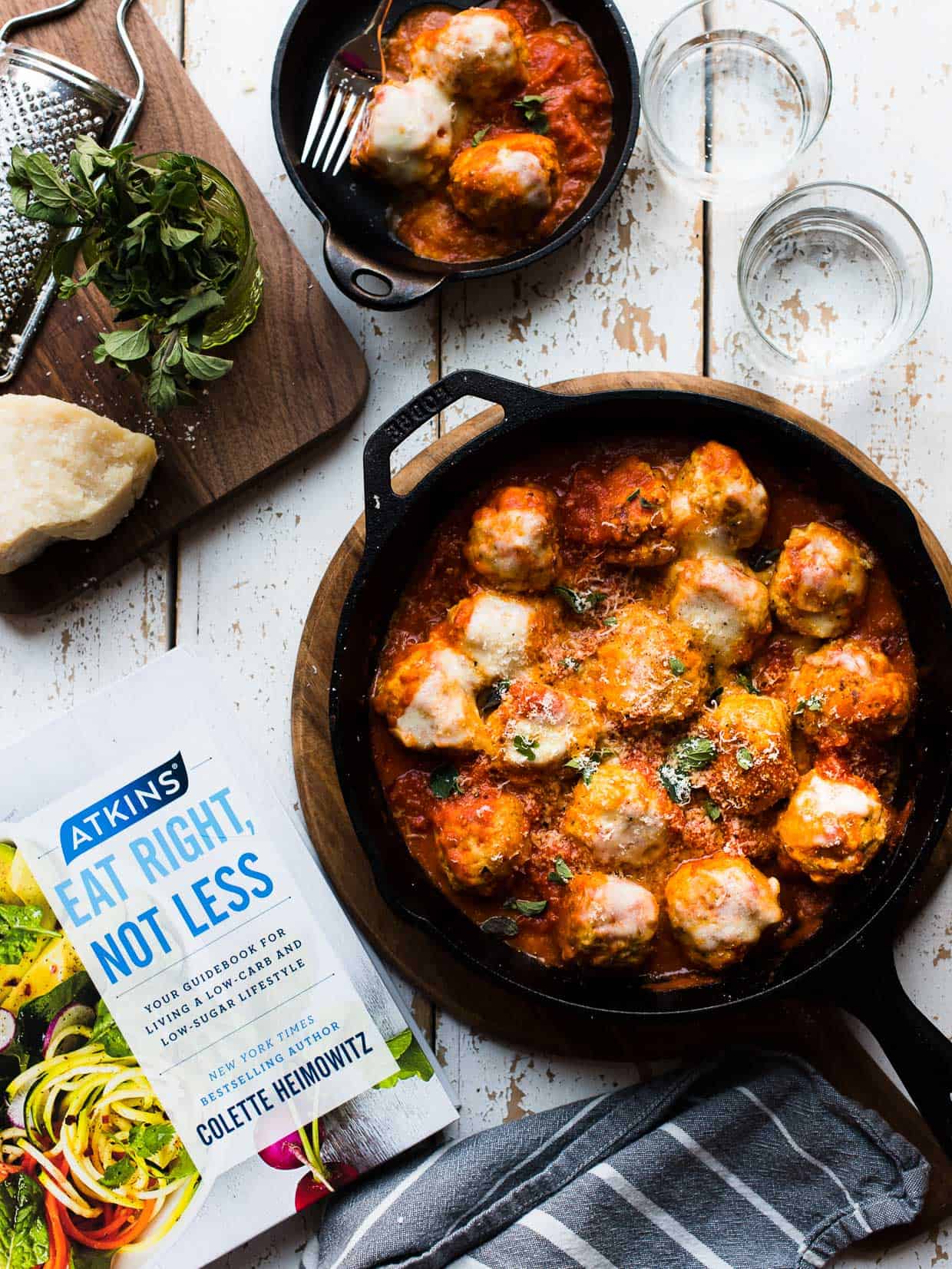 Chicken Parmesan Meatballs in a cast iron skillet next to a copy of Atkins: Eat Right, Not Less guidebook