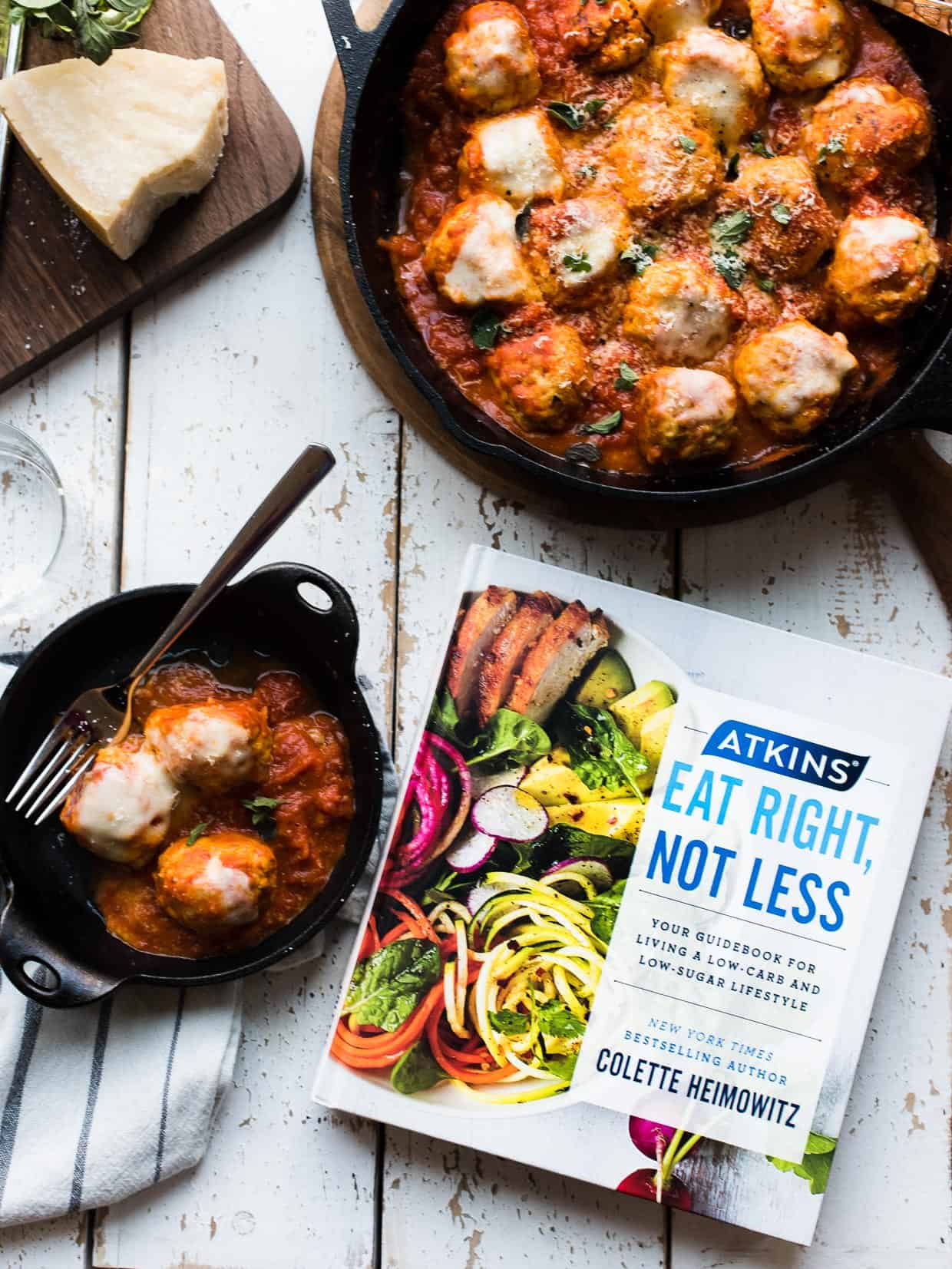 Chicken Parmesan Meatballs in a cast iron skillet next to a copy of Atkins: Eat Right, Not Less guidebook