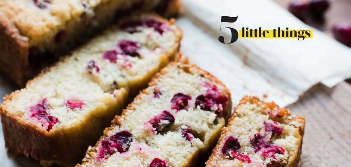 A loaf of cranberry bread cut into slices and served on a wooden cutting board.