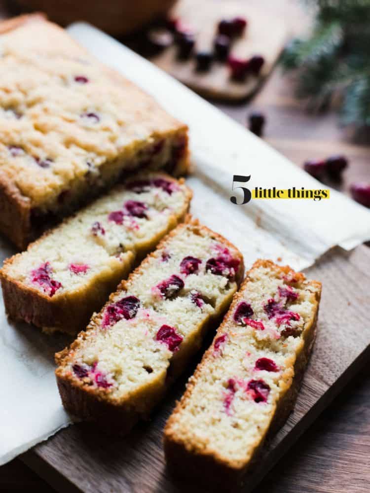 A loaf of cranberry bread cut into slices and served on a wooden cutting board.