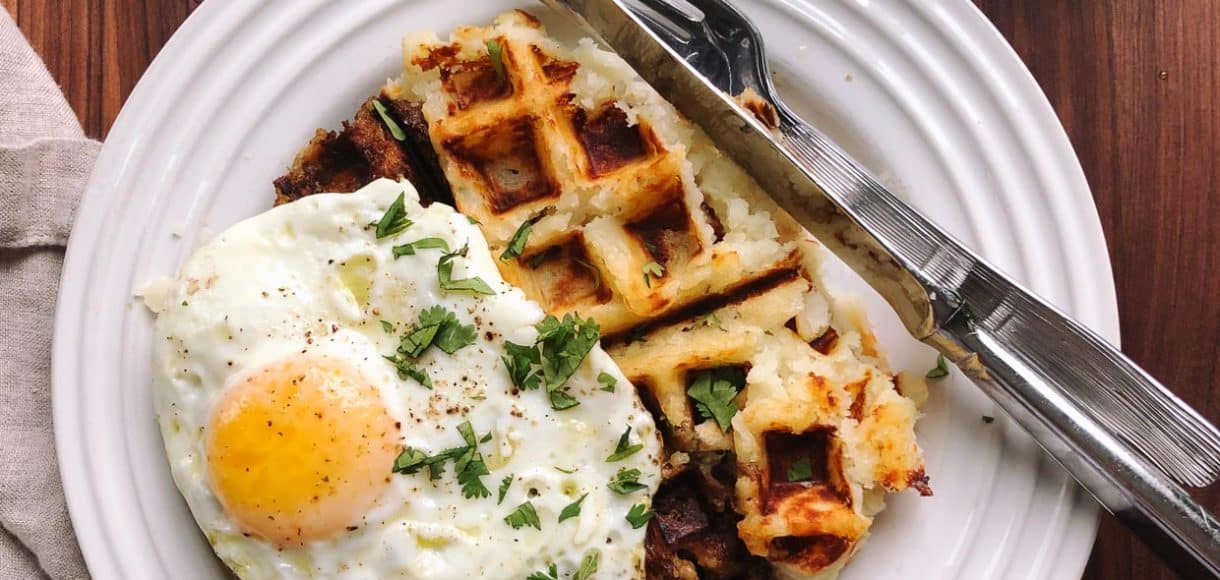 Waffle with a fried egg on top served on a white plate.