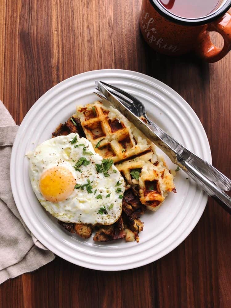 Waffle with a fried egg on top served on a white plate.