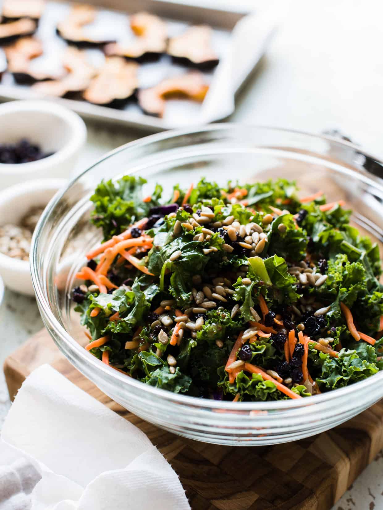 Kale salad with carrots, currants, and sunflower seeds in a glass bowl for Roasted Acorn Squash and Kale Salad.
