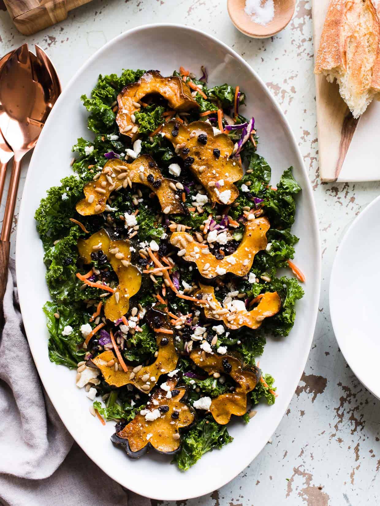 Roasted acorn squash over kale, with sunflower seeds, currants and a maple vinaigrette on a white serving platter.