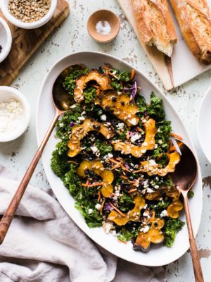 Roasted acorn squash over kale, with sunflower seeds, currants and a maple vinaigrette on a white serving platter.