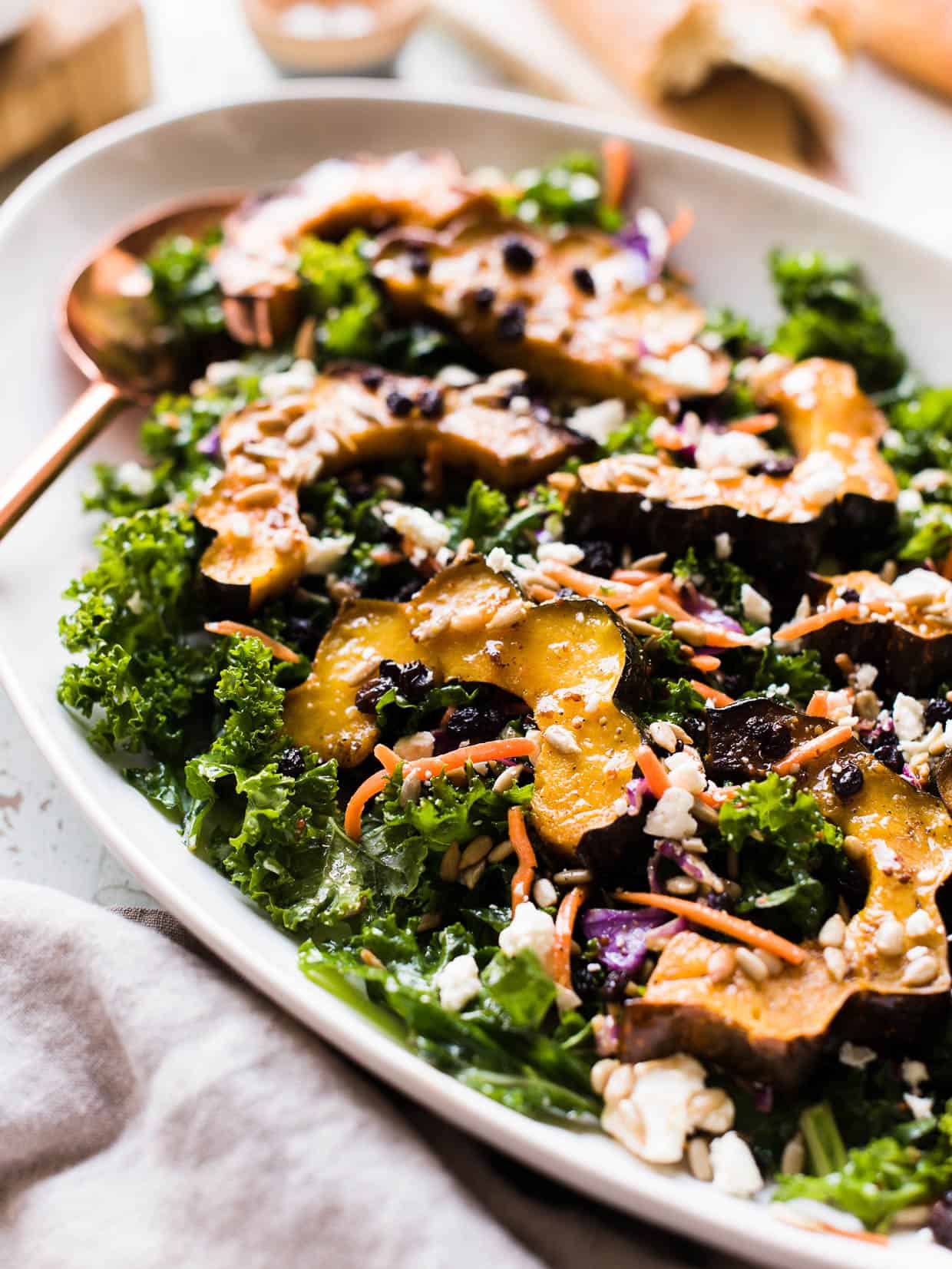 Roasted acorn squash over kale, with sunflower seeds, currants and a maple vinaigrette on a white serving platter.