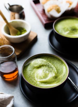 Matcha green tea lattes in black bowls with almond milk, maple syrup.