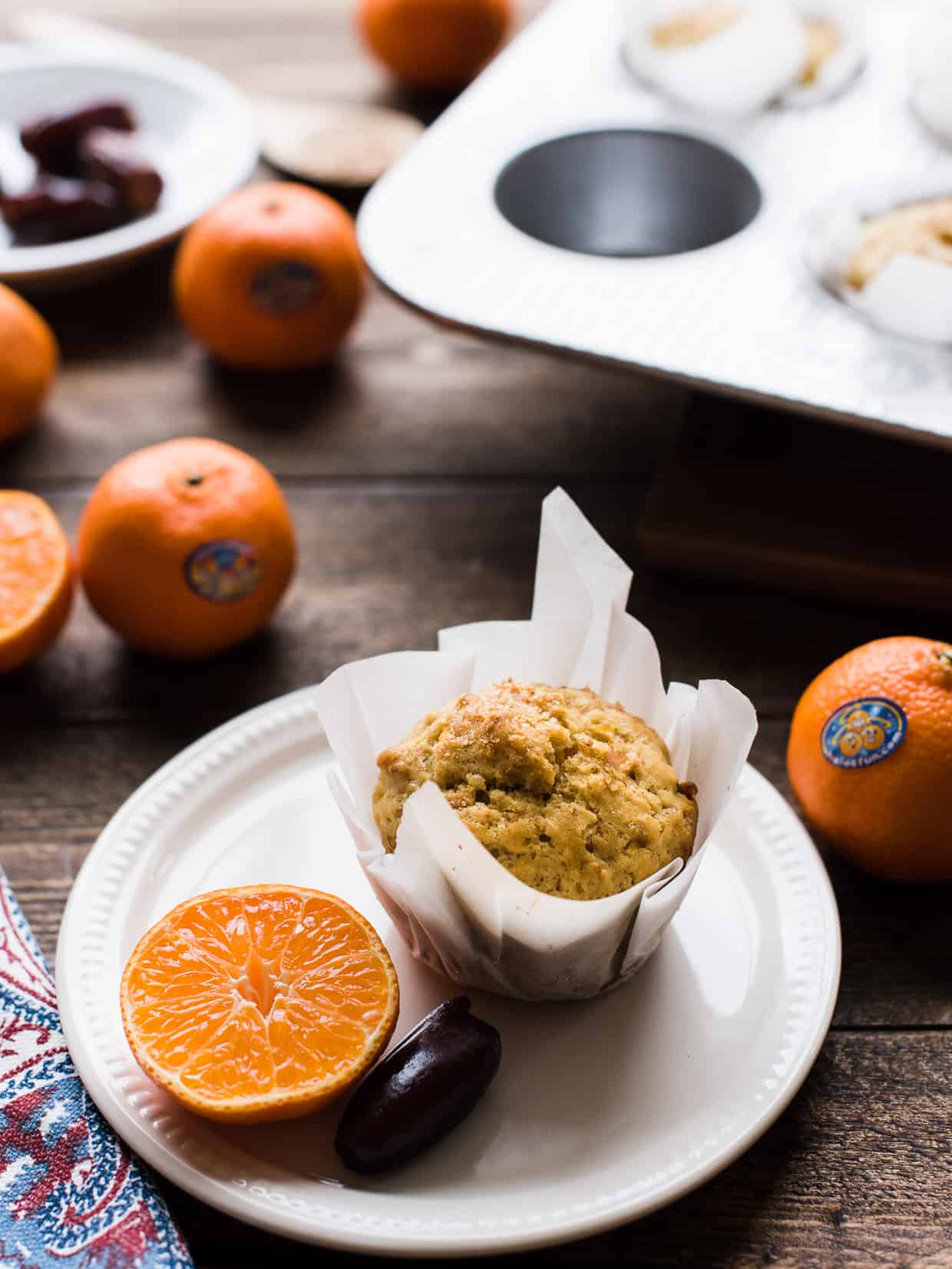 A mandarin orange ginger date muffin on a plate with a segment of mandarin orange.