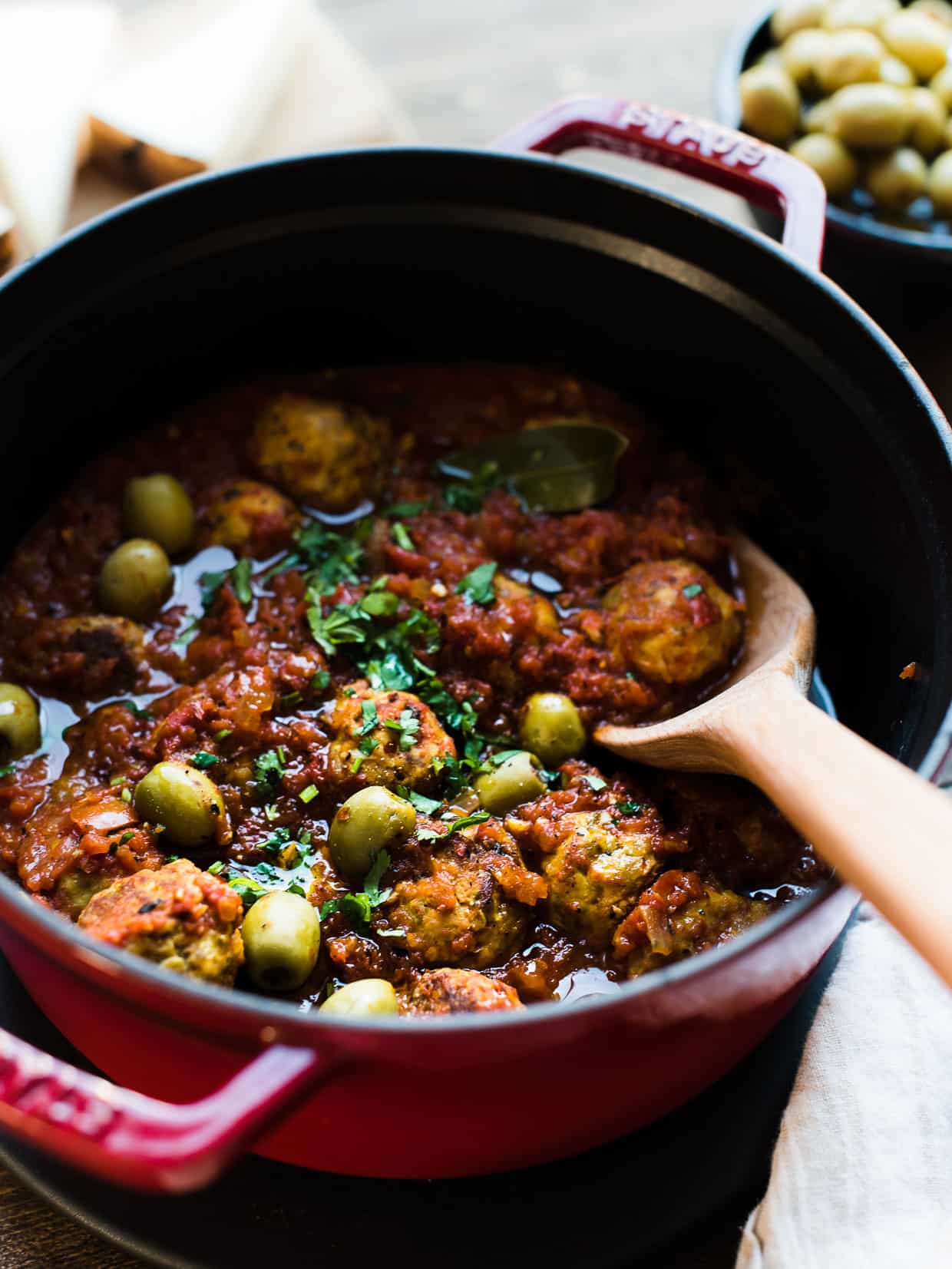 Albondigas with Olives in red Dutch Oven with wooden spoon.