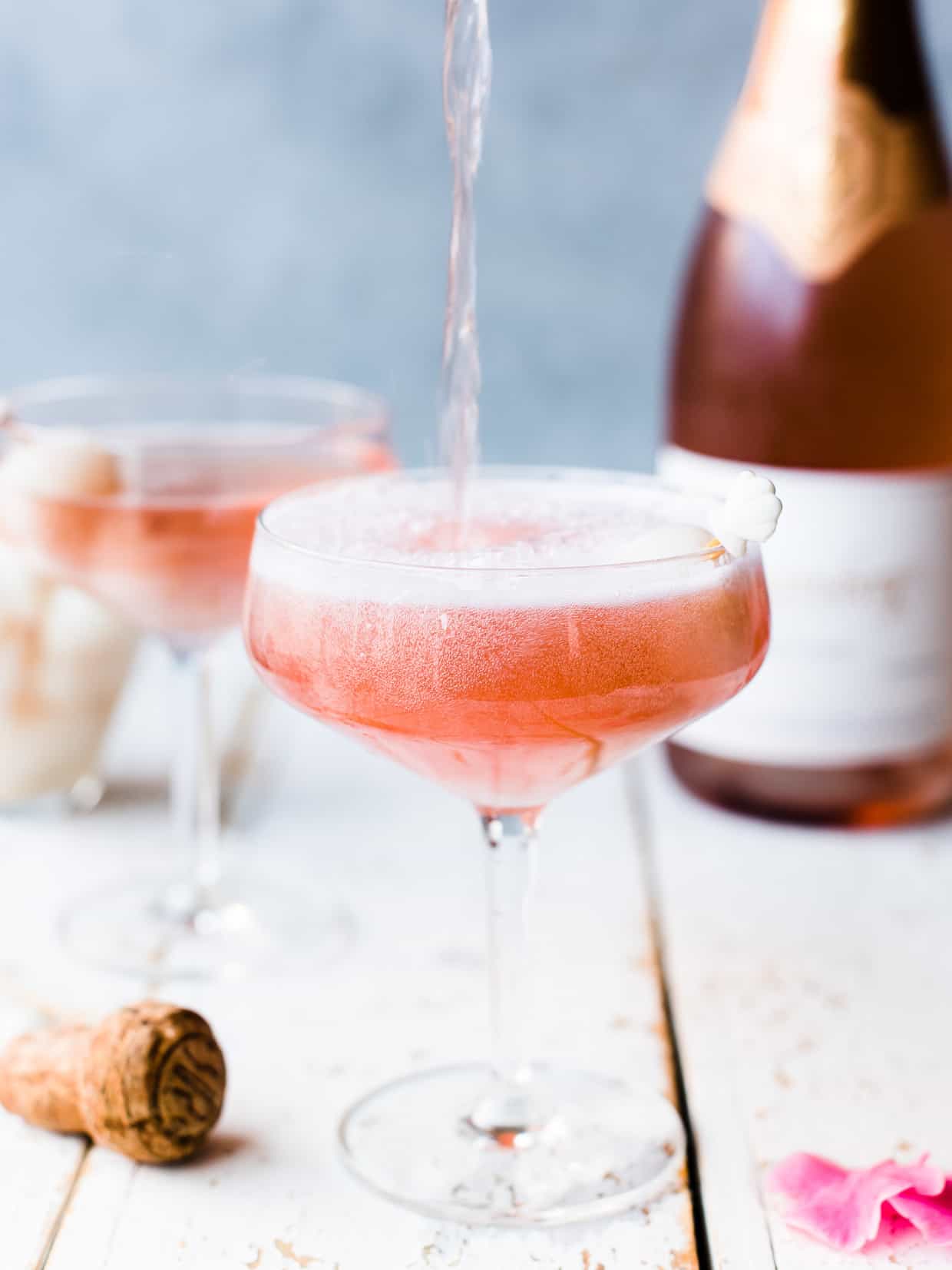 Pink lychee rose mimosa with sparkling wine pouring into glass.
