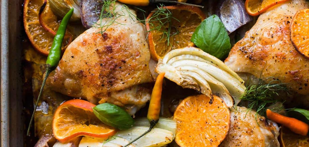 Thai-Spiced Mandarin Orange Roasted Chicken Thighs with thin slices of mandarin oranges, fennel, onion and garlic on a sheet pan.
