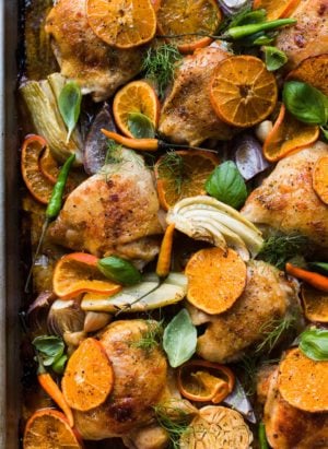 Thai-Spiced Mandarin Orange Roasted Chicken Thighs with thin slices of mandarin oranges, fennel, onion and garlic on a sheet pan.