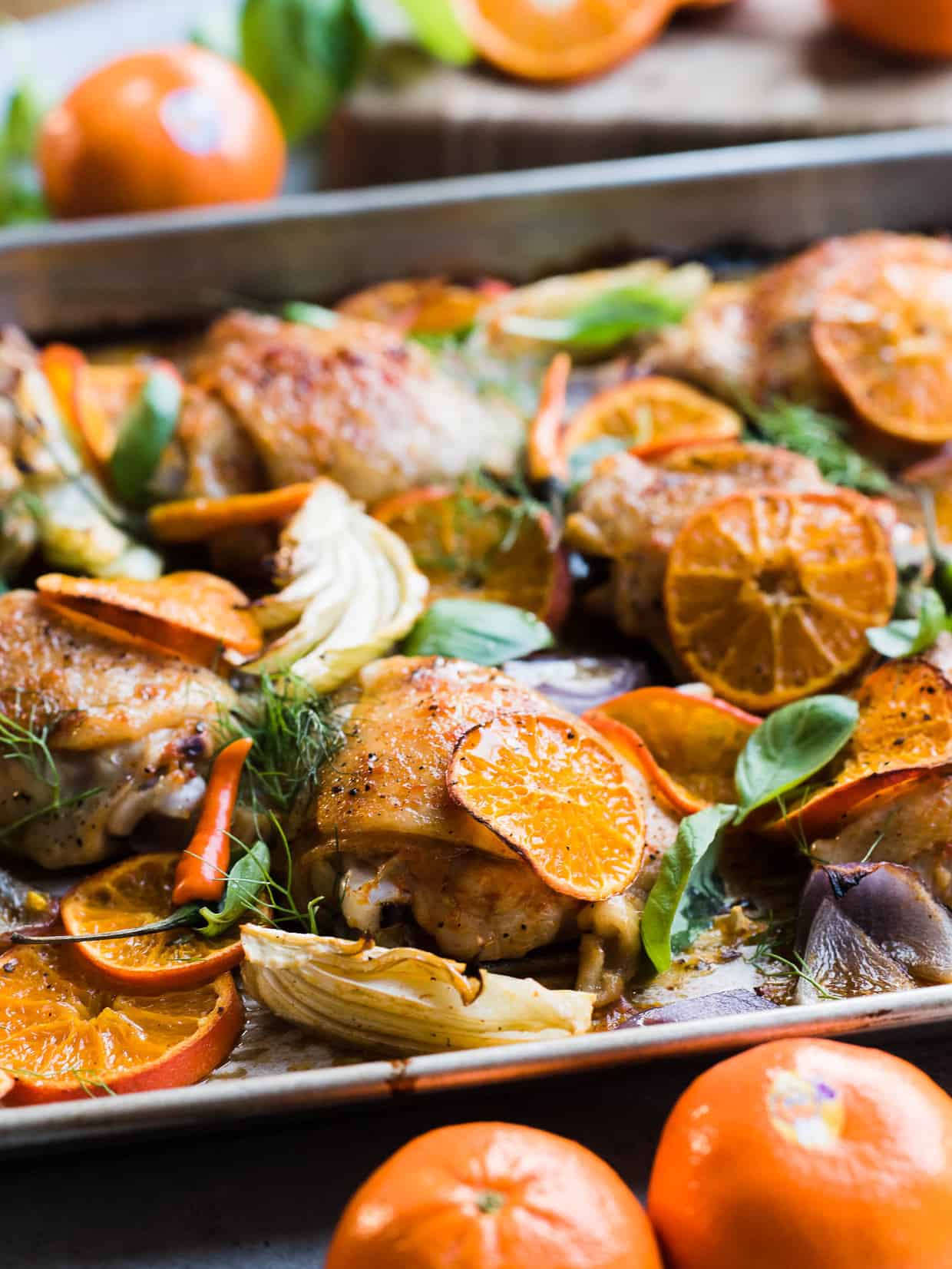 Thai-Spiced Mandarin Orange Roasted Chicken Thighs on a baking sheet with slices of orange, fennel and onion.
