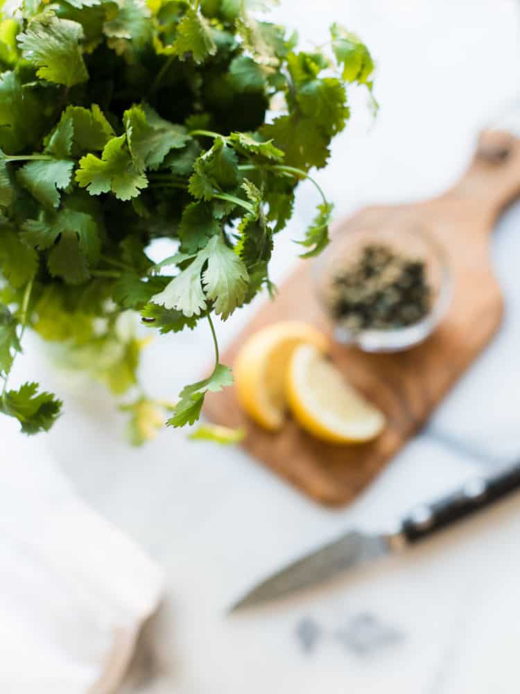 Fresh cilantro with lemons and capers in the background.