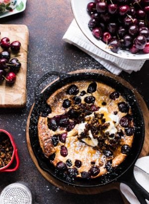 Cherry Dutch Baby Pancake with Pecan Streusel and cream in a cast iron skillet.