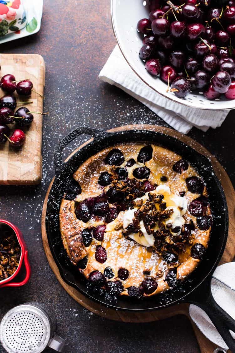 Cherry Dutch Baby Pancake with Pecan Streusel and cream in a cast iron skillet.