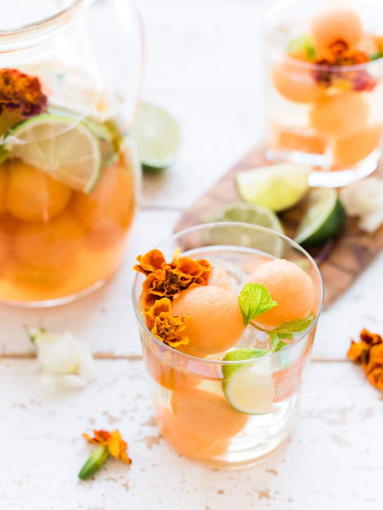 A glass of white sangria with cantaloupe, lime, mint and edible flowers.
