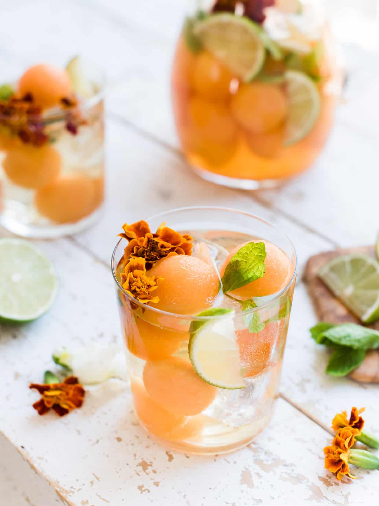 White sangria in a glass with cantaloupe, ginger, lime, mint and edible flowers.