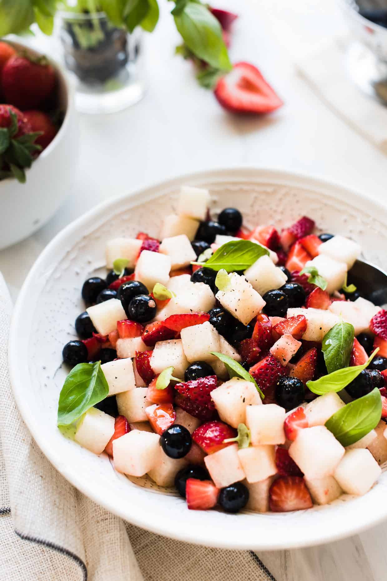 Strawberries, blueberries, and crispy jicama come together for a super simple, patriotic, and barbecue-ready Red, White and Blue Berry Jicama Salad in a white bowl.