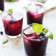 Glasses of blueberry ginger basil soda garnished with basil and blueberries.