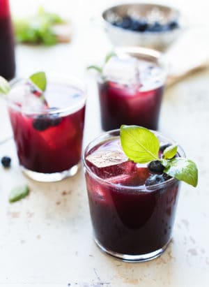 Glasses of blueberry ginger basil soda garnished with basil and blueberries.