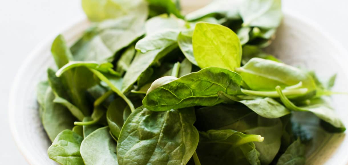 A bowl of fresh spinach on a cloth napkin.