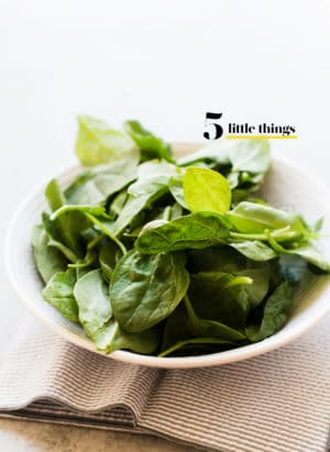 A bowl of fresh spinach on a cloth napkin.