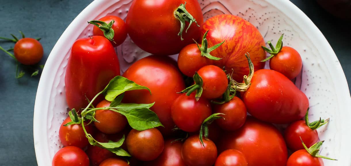 Tomatoes in a white bowl on grey table.