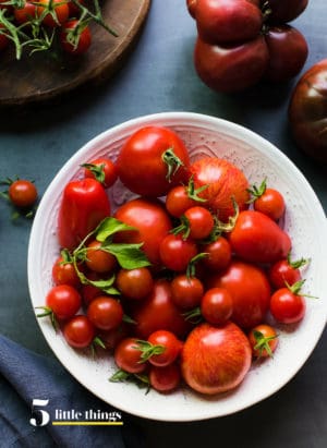 Tomatoes in a white bowl on grey table.