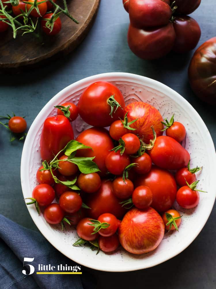 Tomatoes in a white bowl on grey table.