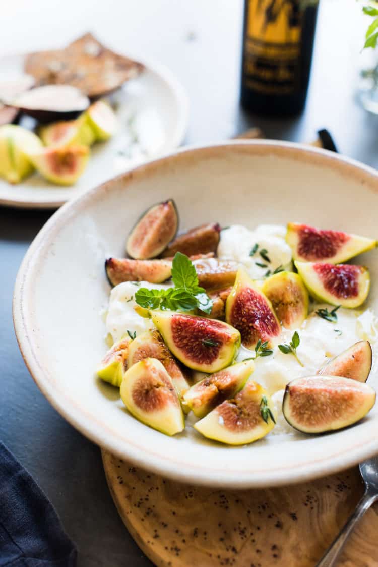 Slices of honey-balsamic figs with burrata with fresh mint and thyme in a bowl. 