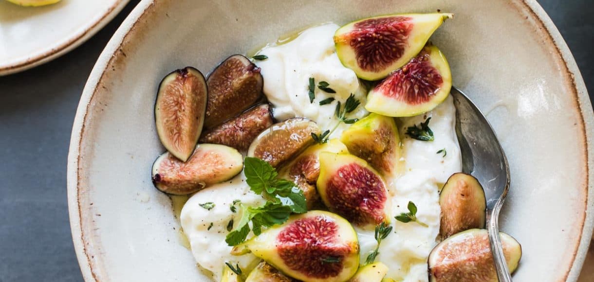 Slices of honey-balsamic figs with burrata with fresh mint and thyme in a bowl.