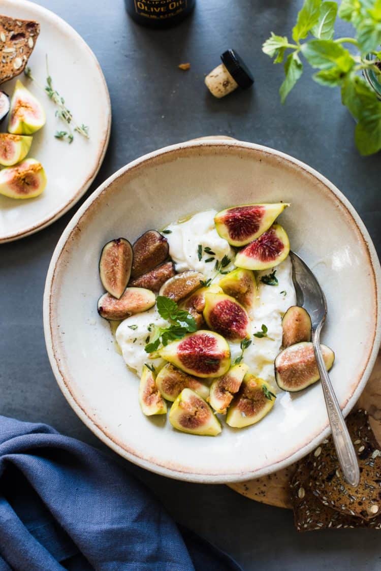 Slices of honey-balsamic figs with burrata with fresh mint and thyme in a bowl.