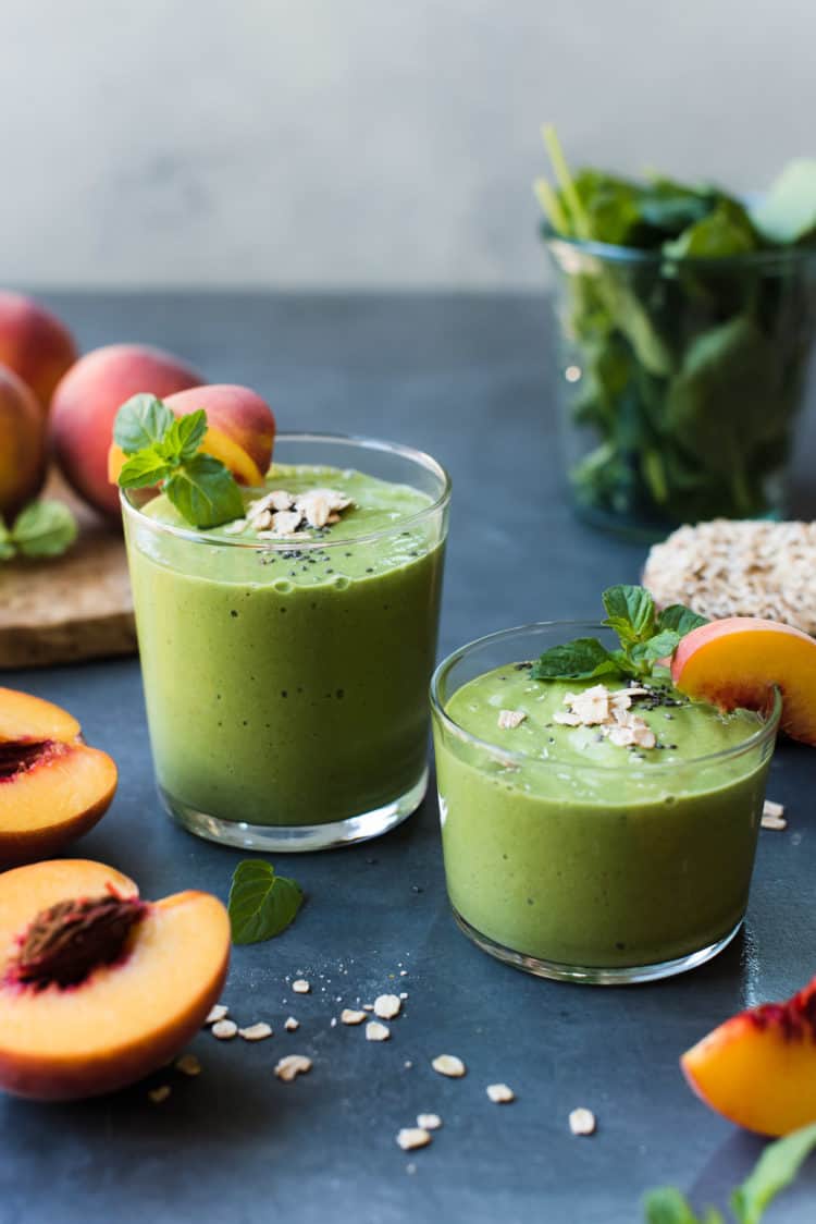 Glasses of Peaches and Cream Green Breakfast Smoothie with slices of peach and spinach in the background.