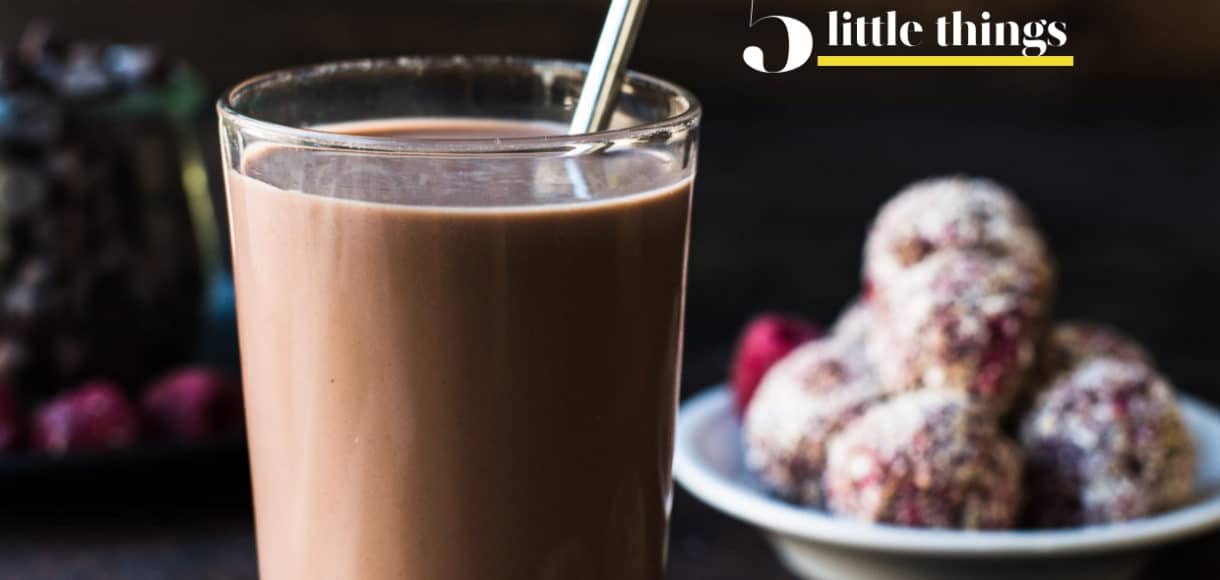 A glass of chocolate milk with a metal straw and energy bites in the background.