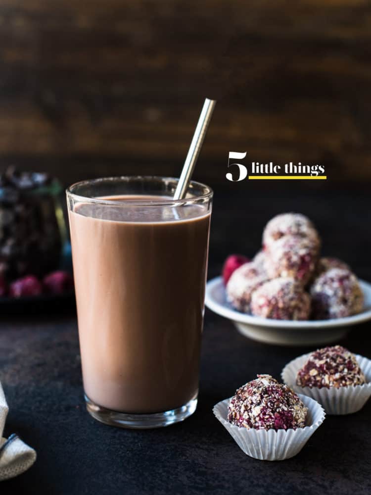 A glass of chocolate milk with a metal straw and energy bites in the background.