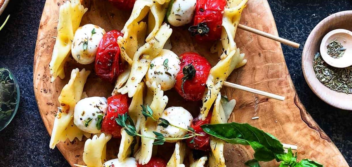 Roasted Tomato Caprese Skewers with pasta on a wooden cutting board.