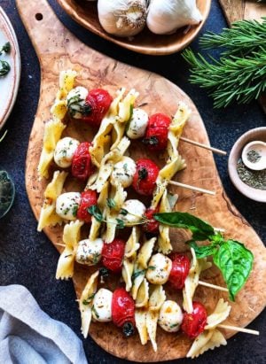 Roasted Tomato Caprese Skewers with pasta on a wooden cutting board.